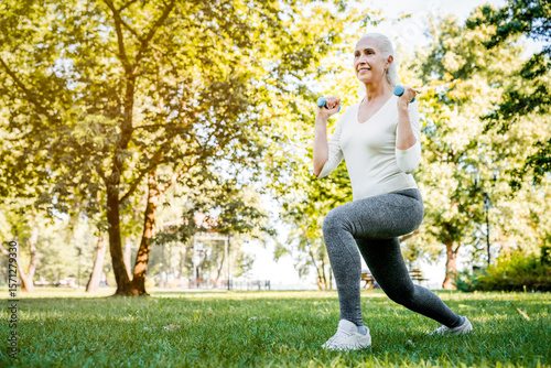 Full length of senior woman retired person enjoys workout, exercises with dumbbell, training body in midst of nature, dedicating herself to healthy lifestyle and staying active. Outdoor fitness.