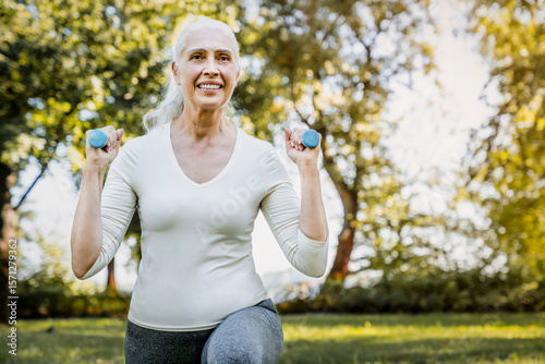 Close up shot of senior woman retired person enjoys workout, exercises with dumbbell, training body in midst of nature, dedicating herself to healthy lifestyle and staying active. Outdoor fitness.