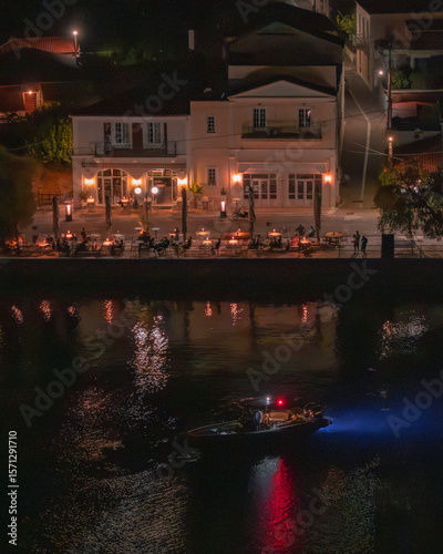Aerial view of the glowing building and the boat reflecting vibrant colors in the water at night, Limni, Euboea, Greece.