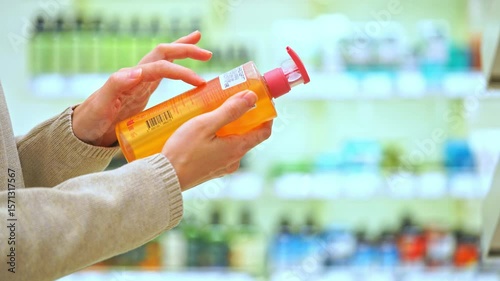 Woman holding a bottle of shampoo or body wash in a beauty store, reading the label, examining ingredients. Close-up of female hands. Concept of conscious choice, haircare, personal skincare awareness