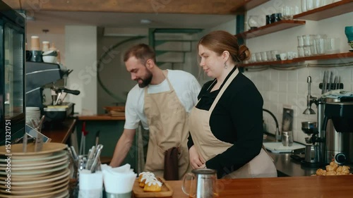 The female owner and male employee put on aprons and put towels in their pockets, then she puts desserts in the display case