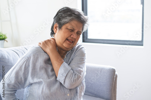 Pain body muscles stiff problem, suffer asian senior woman painful, older hand holding neck ache and aged holding massaging rubbing body, injury hurt,sore sitting on sofa at home. Health care concept.