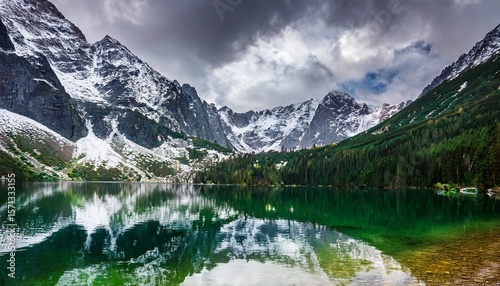 towering snow covered tatra mountains are reflected in the clear emerald waters of morskie oko lake beneath a moody sky near zakopane poland