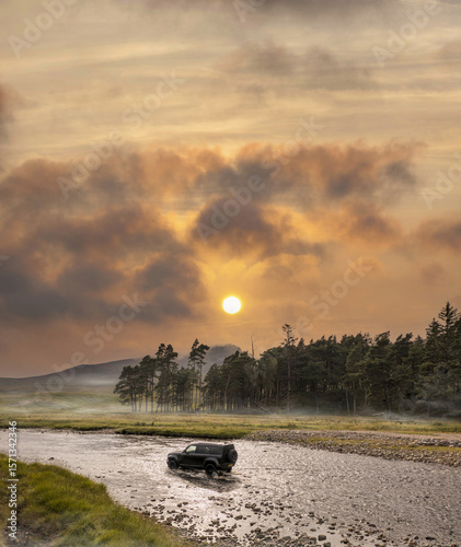 Aerial view of a lone vehicle braving the shallow waters near Ardverikie Estate under a fiery sunset, Newtonmore, Scotland, United Kingdom.