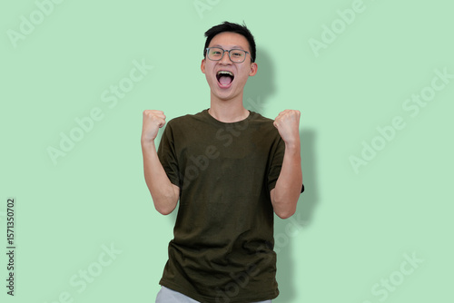 Excited Young Man Celebrating Success with Raised Fists on a Pastel Green Background