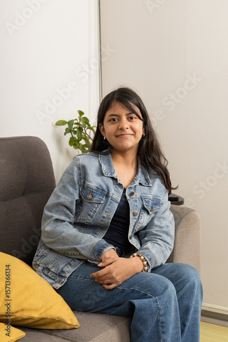 A teenager is sitting on a couch wearing a blue jacket