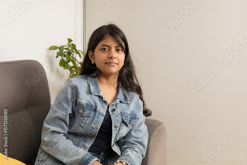 A teenager is sitting on a couch wearing a blue jacket