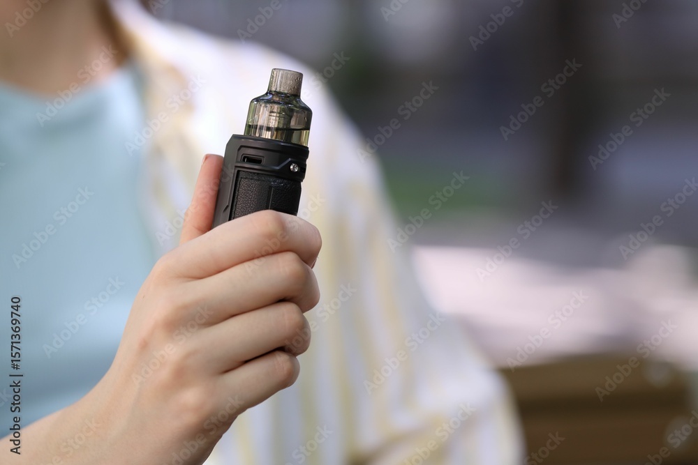 Fototapeta premium Young woman with electronic smoking device outdoors, closeup. Space for text