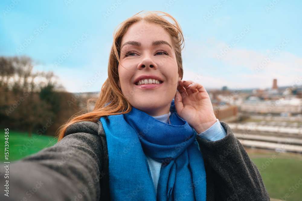 Smiling woman takes a selfie outdoors with a scenic view in the background during a bright and windy day Smiling woman takes a selfie outdoors with a scenic view in the background during a bright and windy day