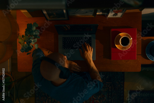Portrait of a young caucasian man wearing wireless headphones using a laptop sitting in a cosy living room, top view.