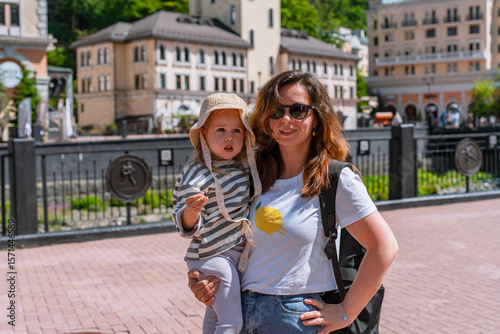 Family mother and little child 3 year in Rosa Khutor resort, buildings and river at the foot of the mountains. Sochi, Russia - 8 June 2025