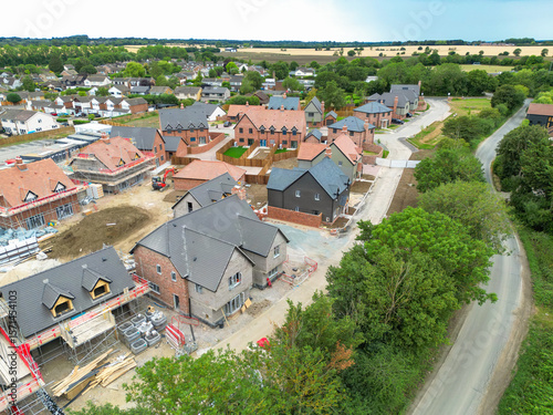 Aerial view of nearly completed, expensive and detached family homes seen on a housing development site in rural Essex, UK. A country lane snakes passed to the development to a nearby old village.