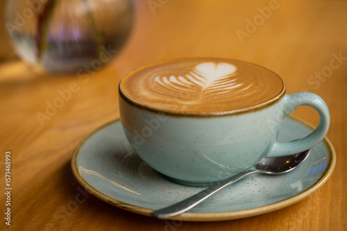 Close-up of cappuccino with latte art in pastel blue ceramic cup on rustic wooden table. Cozy, minimalist coffee scene, ideal for morning rituals and coffee shop lifestyle.