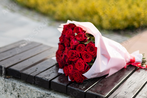 A romantic bouquet of red roses resting on a rain-dampened bench in a quiet park, symbolizing love, waiting, or a missed meeting.