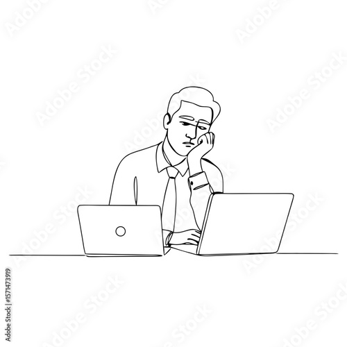 Young man looking bored while working on two laptops at desk  