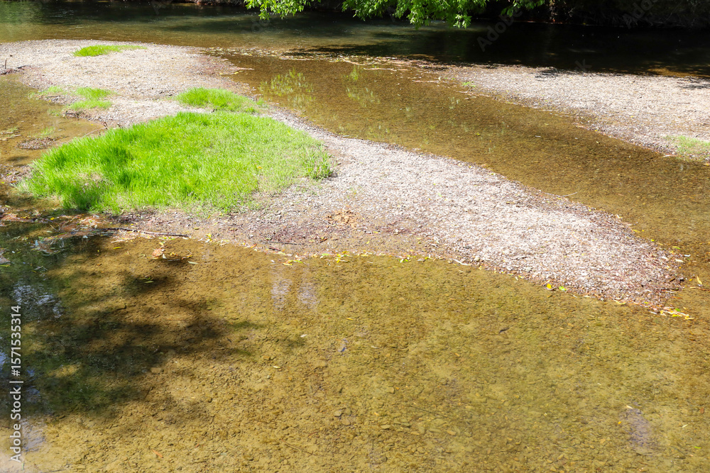 Ταπετσαρία A section of a river with shallow water revealing a pebbly bottom and an islet of vibrant green grass