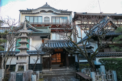 Fototapeta Naklejka Na Ścianę i Meble -  A serene courtyard in Nagano, Japan, features a small stone pagoda, bare winter trees, and traditional buildings, evoking a sense of tranquility and the quiet beauty of Japanese design aesthetics.