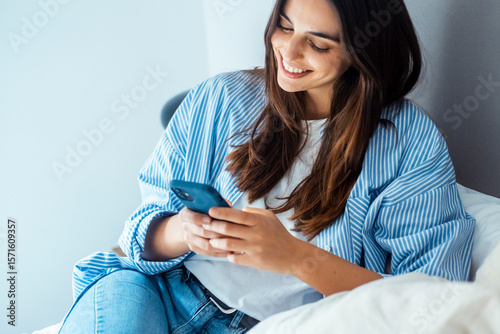 Smiling young woman using smartphone to browse, chat, and connect online. Modern lifestyle with technology, social media, messaging apps, online shopping, web search, and digital communication