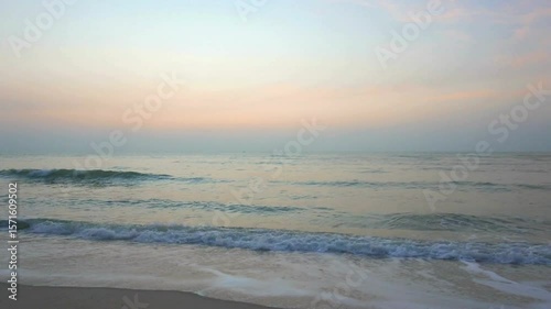 Gentle waves roll onto the sandy beach at sunrise