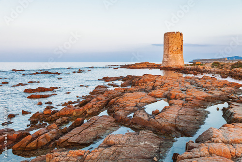 Ancient coastal watchtower on rocky shore at sunset with calm sea and soft twilight sky