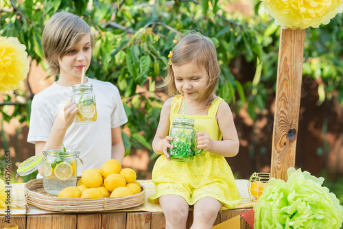 Children drink natural lemonade at stand in park. Summer refreshing natural drink lemonade. Detox fruit infused flavored water, cocktail in a beverage dispenser with fresh fruits