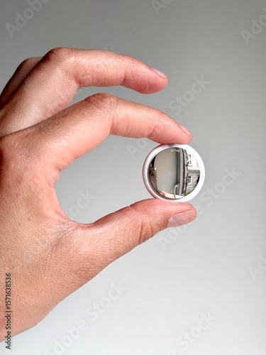 Hand holding an Apple AirTag tracker device with reflection on surface. Minimalist technology concept on light background