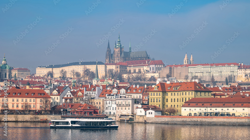 Fototapeta premium Panoramic view of Prague Castle complex towering over historic Lesser Town and Vltava River. Tour boat. Prague, Czech Republic - February 24, 2025