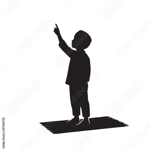 Young muslim boy in silhouette praying on a mat pointing towards a mosque dome