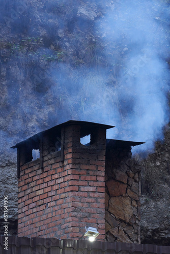 Brick rectangular chimney with billowing white smoke against the backdrop of a steep cliff. Copy space.