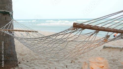 A hammock hangs between palm trees on a sandy beach by the ocean
