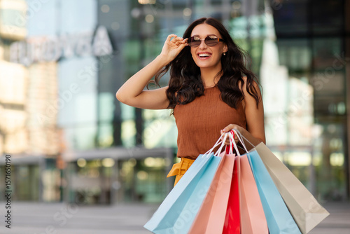Stylish happy lady with shopping bags walking down the street, going from the mall, carrying purchases and smiling, free space