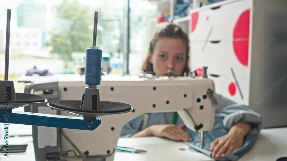 A close-up of a spool of thread, used for sewing denim clothing in a tailor's workshop, while operating a sewing machine.