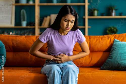 Woman experiencing stomach pain sitting on couch home remedies for abdominal discomfort and cramps relief tips