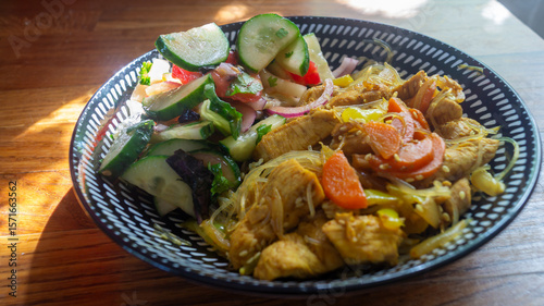A dish with rice noodles and vegetable salad in a deep bowl on a wooden table