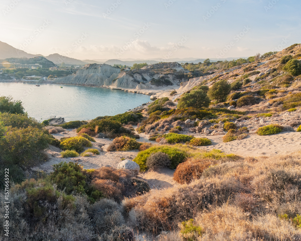 Obraz premium Earth and light in quiet rhythm — sun-kissed coastal hills and textured vegetation unfold toward a serene bay, inviting mindful exploration in Mediterranean stillness. Greece, Rhodes island