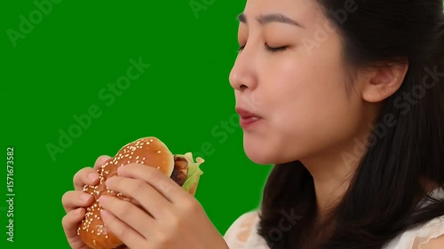 Woman enjoys delicious burger with fresh toppings in a green screen setting