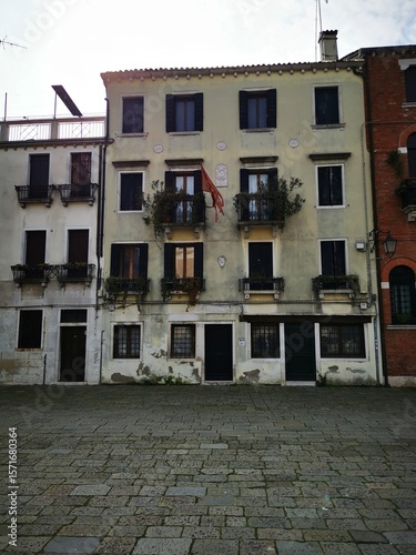 Historic buildings with balconies adorned with plants in a quiet Venetian square under a clear sky