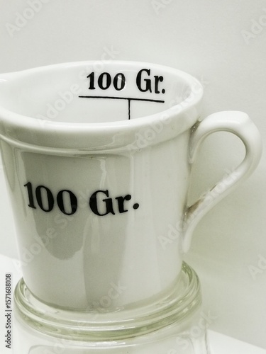 Ceramic measuring cup indicating 100 grams displayed on a glass surface for cooking demonstration or kitchen use