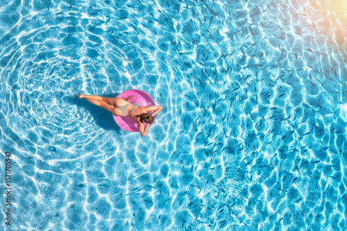 Aerial view of a young woman swimming with pink swim ring in blue sea with school of fish at sunset in summer. Tropical landscape with girl, clear water, sandy beach in Greece. Top view. Travel