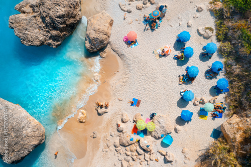 Aerial view of blue sea, sandy beach with umbrellas, stones and rocks in water at sunset in summer. Lefkada island, Greece. Tropical landscape with sea coast, swimming people, blue water. Top view