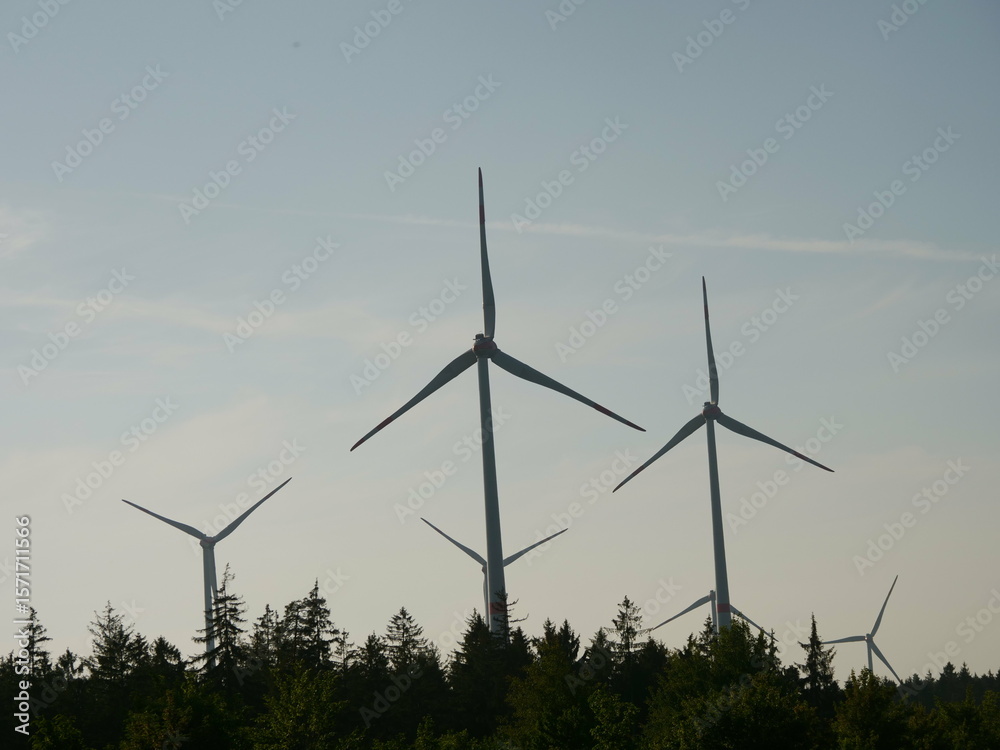 Group of wind turbines are in the sky, with the sun setting behind them Group of wind turbines are in the sky, with the sun setting behind them