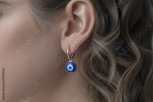 Close up shot of a woman's ear wearing a gold hoop earring with a blue evil eye charm pendant