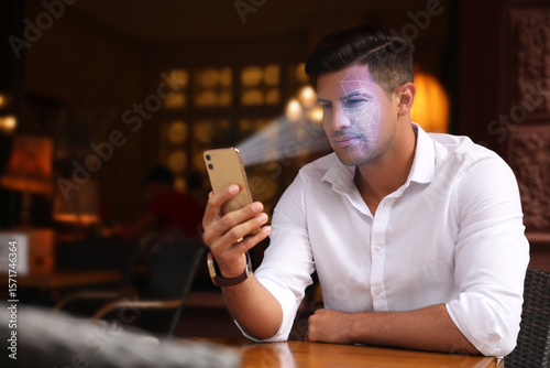 Fotografie Man unlocking his smartphone with facial recognition app in cafe