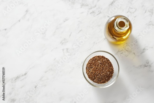 Top-down shot showing flax seeds in a glass bowl and a bottle of flaxseed oil on marble.