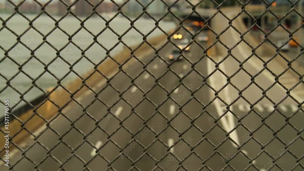 Cars drive on the highway seen through a chainlink fence
