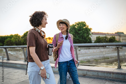 two women friends with suitcases discuss and walk on bridge