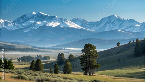 Landscape view of snow capped mountains with green hills and trees under a clear blue sky