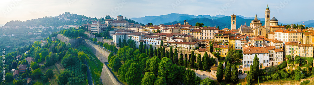 Obraz premium Aerial view of Bergamo’s Città Alta in Italy with terracotta rooftops, historic churches, and mountain backdrop on a clear day