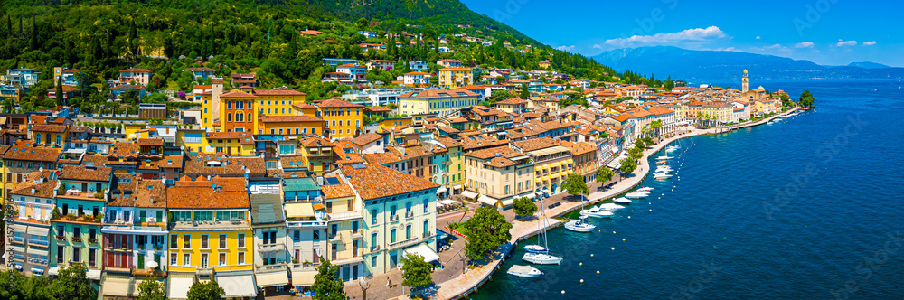 Fototapeta premium Aerial view of Salo, Italy with terracotta rooftops, lakeside promenade, and boats docked on the shore of Lake Garda on a sunny summer day