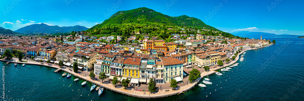 Fototapeta premium Aerial view of Salo, Italy with terracotta rooftops, lakeside promenade, and boats docked on the shore of Lake Garda on a sunny summer day
